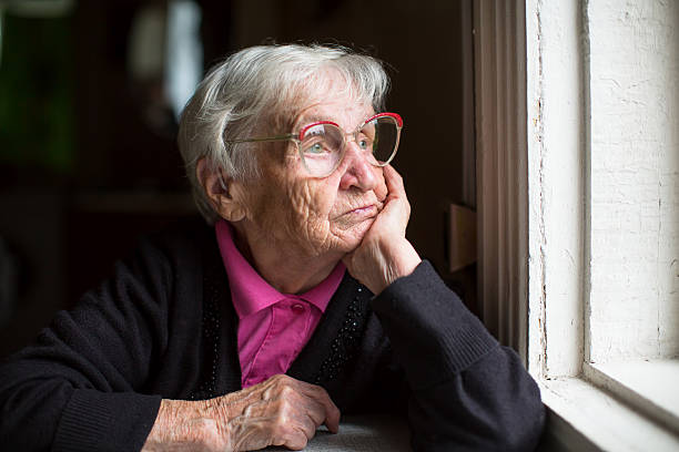 Elderly woman in glasses thoughtfully looking out the window. stock photo