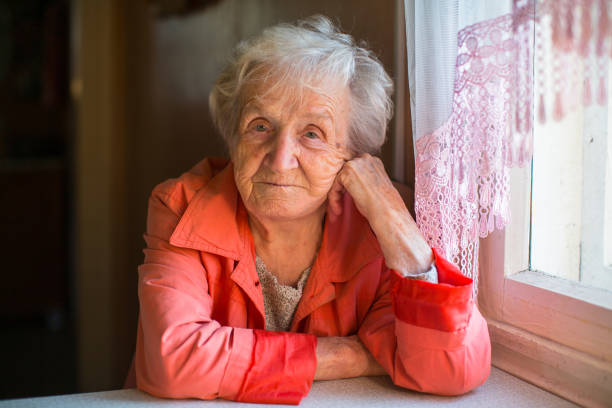 Elderly woman in red jacket sitting at the table in the house. stock photo
