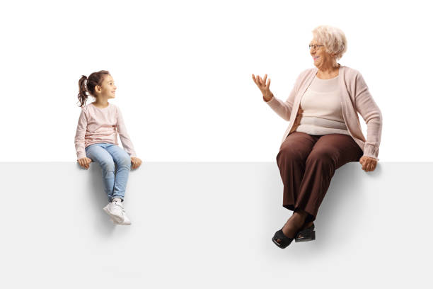 Elderly woman sitting on a blank panel and talking to a little girl stock photo