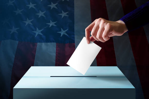 Election in America Concept. Hand Dropping a Ballot Card into the Vote Box, Flag of United States as background Election in America Concept. Hand Dropping a Ballot Card into the Vote Box, Flag of United States as background election photos stock pictures, royalty-free photos & images