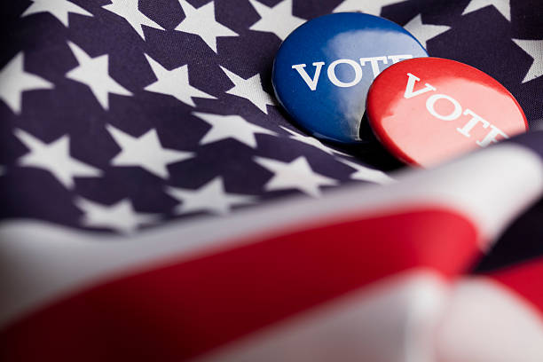 Red and blue election badges with the word vote written in white. The badges are on an american stars and stripes flag