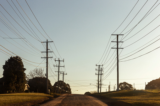 Electric poles with many cables located along rural country road with clear blue sky in background.