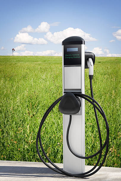 Electric Vehicle Charging Station An Electric Vehicle Charging Station sits at the edge of a field of tall grasses with a windmill far off in the background. Concept image for Greener Energy. battery charger stock pictures, royalty-free photos & images