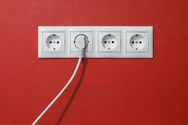 Electrical outlets, cable and electric plug on red textured wall stock photo