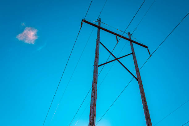 Electricity pole and power cables, and a piece of pink white cloud on turquoise-colored sky background stock photo