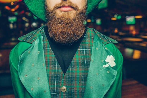 Elegant and calm young man in pub. He wear green suit of saint patrick. Guy has red beard. stock photo
