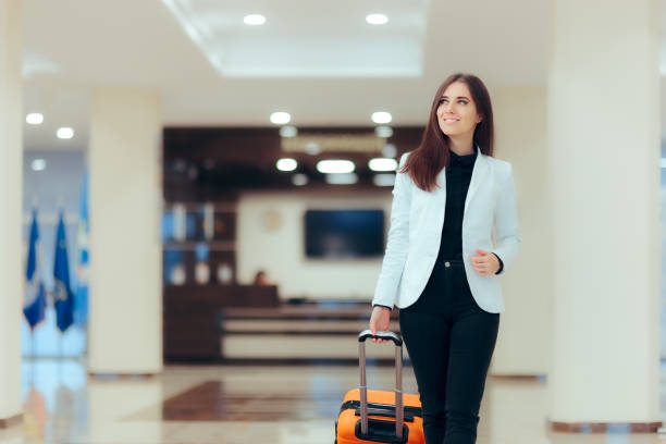 elegant business woman with travel trolley luggage in hotel lobby - airport lounge business imagens e fotografias de stock