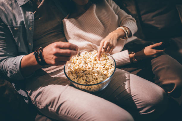 Elegant couple watching movie together and eating popcorn Close-up of chic couple's hands watching television and eating popcorn at night wundervisuals stock pictures, royalty-free photos & images