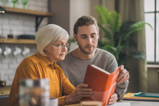 Elegant good-looking grey-haired woman and her son reading a book New book. Elegant good-looking grey-haired woman and her son reading a book linguistics stock pictures, royalty-free photos & images