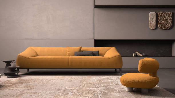 Elegant grunge living room with plaster walls and floor, fireplace. Orange sofa with pillows, carpet, fluffy armchair, side tables, vases, decors. Modern interior design idea stock photo