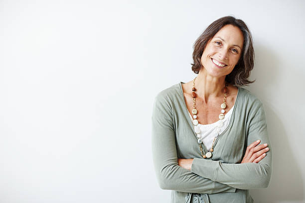 elegant middle aged woman with her arms crossed against white - woman smiling stockfoto's en -beelden