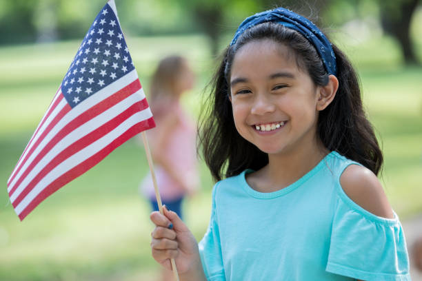 Elementary age Asian little girl smiles while holding American flag Elementary age Asian little girl smiles while holding American flag outdoors on sunny day philippines girl stock pictures, royalty-free photos & images