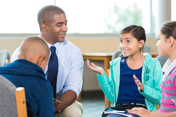 Elementary age kids talking to counselor during group therapy session Diverse group of elementary age little girls and little boys are sitting in circle with mid adult African American male counselor or therapist. Mental health professional is leading children's group therapy session. Children are smiling and talking expressively. school counselor stock pictures, royalty-free photos & images