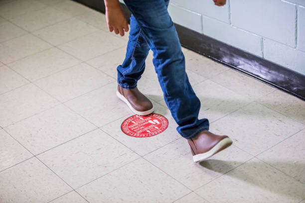 Elementary school student in hallway social distancing Cropped view of an elementary student walking in a school hallway. He has returned to the classroom during the covid-19 pandemic. Stickers on the floor are used to keep the children six feet apart according to social distancing guidelines. feet unit of measurement stock pictures, royalty-free photos & images