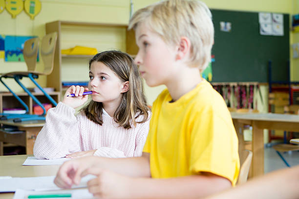 Elementary Students sit in classroom, looking at the board, concentrated stock photo
