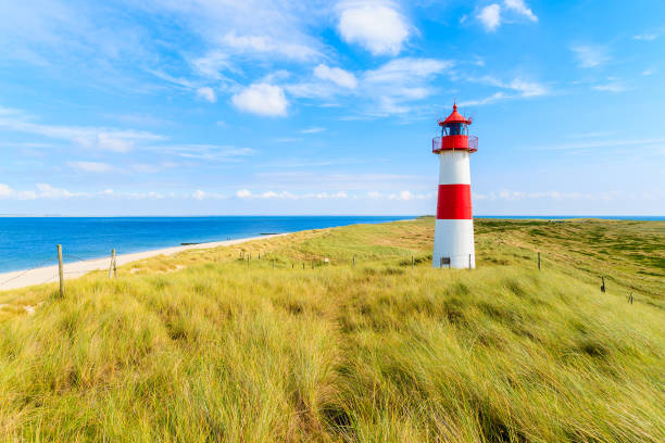 Ellenbogen lighthouse on sand dune against blue sky with white clouds on northern coast of Sylt island, Germany stock photo