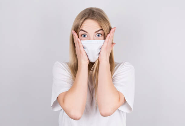 Embarrassed Young caucasian woman wearing medical mask standing over isolated white background, with shocked expression. stock photo