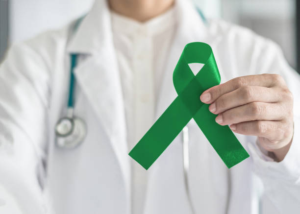 emerald green or jade color ribbon in doctor's hand symbolic for liver cancer and hepatitis b disease awareness concept - world cancer day imagens e fotografias de stock