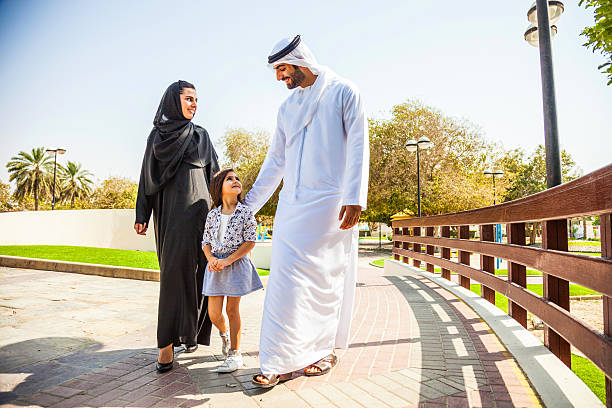 Emirati family in Dubai - enjoying weekend Traditional Emirati young family enjoying the weekend outdoor during a sunny day. The man in front wearing the dishdash traditional wear, the woman wearing the traditional abaya all black dress. arabia stock pictures, royalty-free photos & images