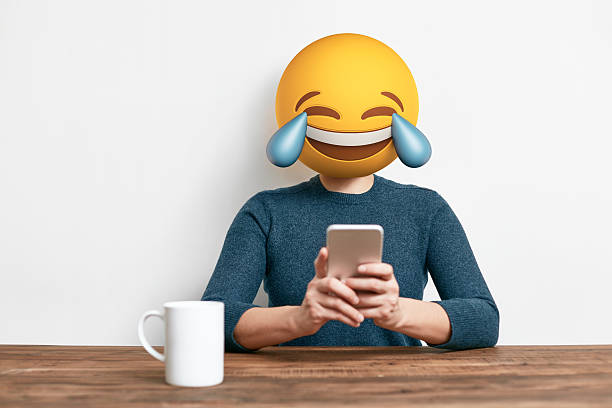 Emoji Head Woman using smart phone Emoji Head Woman sitting at the desk. Woman wearing tears of joy emoji masks while looking at her phone. This emoji is laughing so much that it is crying tears of joy laughing emoji stock pictures, royalty-free photos & images
