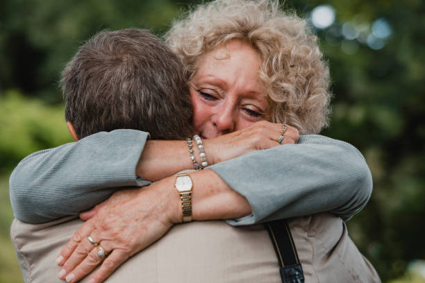 A close-up of an emotional senior female embracing an unrecognizable​ male. she has her arms wrapped around him as they stand outside.