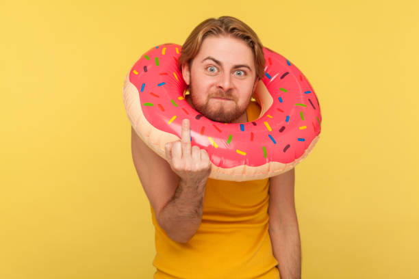 turista emotivo in mutande in piedi con anello di gomma ciambella rosa intorno alla testa e mostrando il dito medio - unkind foto e immagini stock