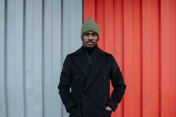 Emotionless black man in a warm autumn coat standing in front of corrugated wall stock photo