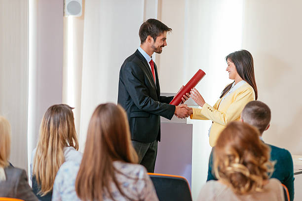 Employee of the month received award on ceremony Image of large or medium group of people sitting in conference hall, and listening to lecturer or professor, actively participating in the class by raising hands, clapping, voting or discussing. Image taken with Nikon D800 and 50 or 85mm lens, developed from RAW. Location: Europe business associate degree? stock pictures, royalty-free photos & images