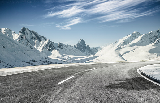 empty asphalt road leading towards snow mountains
