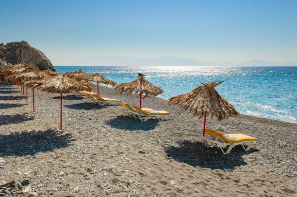 Empty beach with palm leaf umbrellas and lounge chairs on Greek island of Kos stock photo