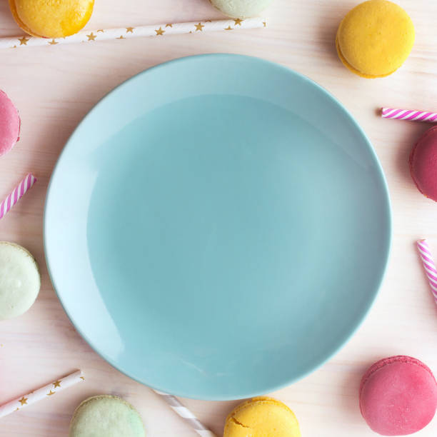 Empty bright blue plate, with a delicious dessert around, macaroons and tubes for a cocktail. Place for text. Festive layout, template. stock photo