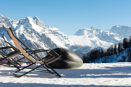 Empty deckchairs stand in the snow against the backdrop of snow-capped mountains. The concept of vacation, landscape.