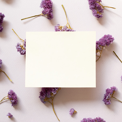 Empty memo note with dry statice flowers on purple background. Floral composition, flat lay, top view, copy space