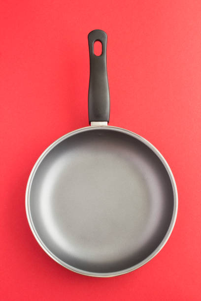 Empty metal frying pan on the red background. Close-up. Copy space. stock photo