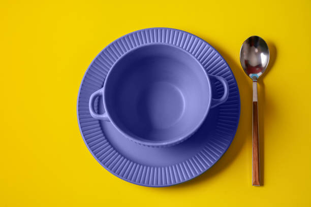 Empty plate of Very Peri color - color of the year 2022 and spoon over background. stock photo