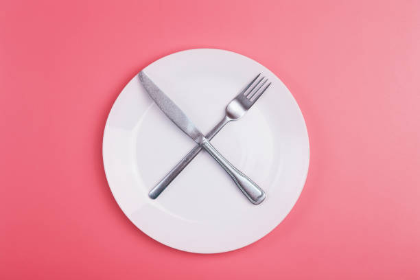 Empty plate on a pink minimal background. Empty white ceramic plate with knife and fork on the table after eating. Diet and healthy food concept. stock photo