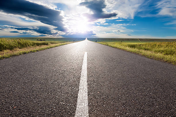 Empty road leading towards the sun Driving on an empty road to the sun dividing line road marking photos stock pictures, royalty-free photos & images