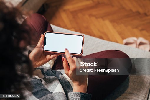 istock Empty Smartphone Screen Held by an Unrecognizable Woman Sitting on the Sofa 1331166339