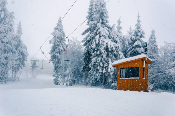 Empty t-bar lift and wooden building at snowfall Snowy ski area: empty t-bar lift and wooden cabin at bad winter weather with snow, wind and fog t bar ski lift stock pictures, royalty-free photos & images