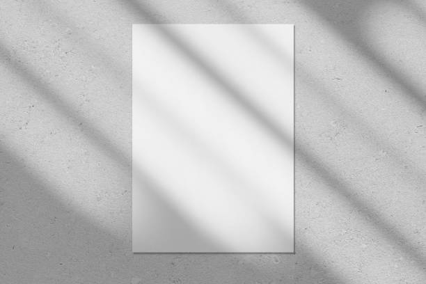 Empty white vertical rectangle poster mockup with diagonal window shadow on the wall Empty white vertical rectangle poster or business card mockup with diagonal window shadow on the smooth gray concrete wall.Flat lay, top view. For advertising, brand design, stationery presentation. poster stock pictures, royalty-free photos & images