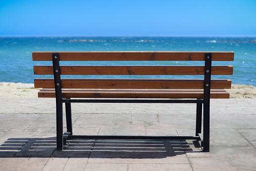 Empty wooden rest bench at sea shore by sunny summer day