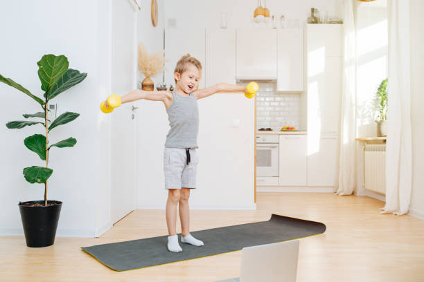 Energetic boy exercising with dumbbells in front of laptop withinstructions stock photo