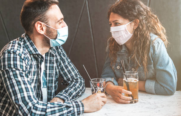 코로나바이러스 전염병 동안 수술용 마스크를 가진 카페 바에 앉아 있는 약혼한 부부 - 예방 및 사회적 단절 개념 - 로맨스 뉴스 사진 이미지