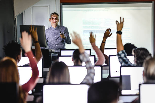 Engaging class at computer lab! Happy mid adult professor asking his students to answer the question on a class at computer lab. computer training stock pictures, royalty-free photos & images