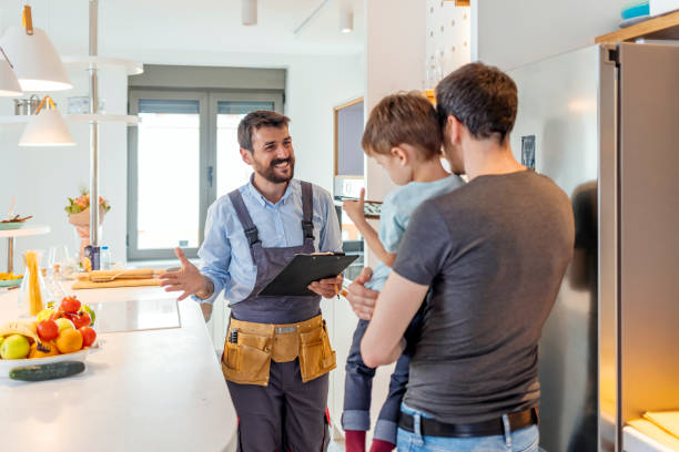 Engineer Giving Advice On Kitchen Repair Professional plumber in uniform talking to male client and his small son indoors. building contractor stock pictures, royalty-free photos & images