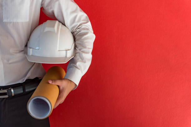 engineer or architect holding safety helmet and architectural drawing in red background - planear obras vermelho imagens e fotografias de stock