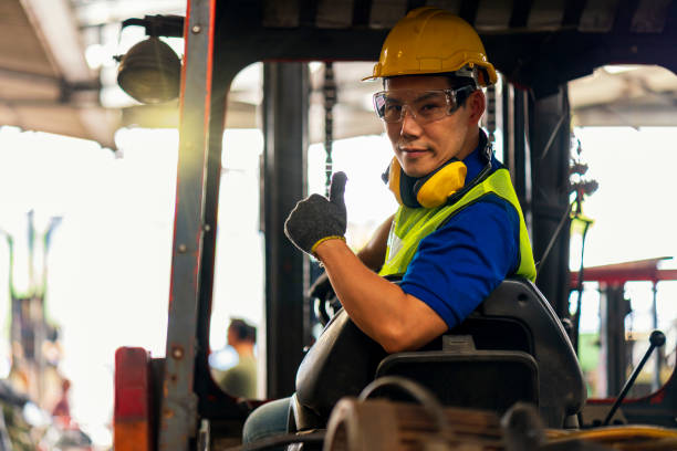 engineer or technician concept. a male employee driving a forklift and showing thumb up in factory. - forklift imagens e fotografias de stock