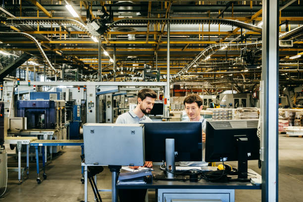 Engineers behind several Computer Monitors in a huge factory stock photo