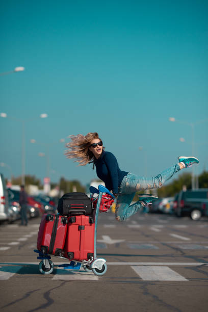 enjoy every trip side view of cheerful tourist woman carrying her suitcases and jumping. luggage cart stock pictures, royalty-free photos & images