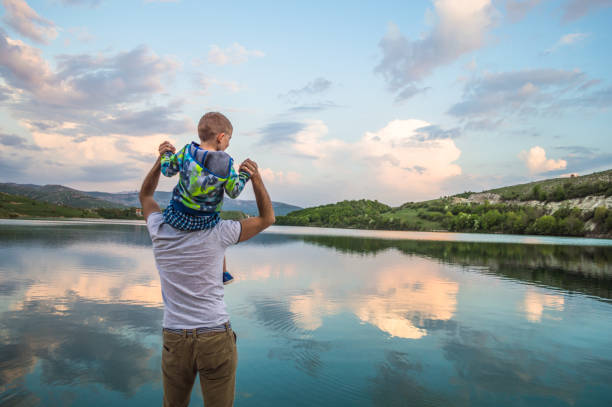 Enjoying a nature Father and son having a great time at the lake. They are smiling and playing. Lake, clouds and nature are behind them. fathers day stock pictures, royalty-free photos & images